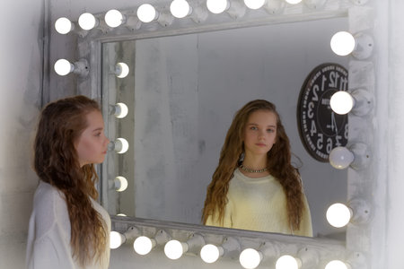 Portrait of a girl in a white sweater in the backlit mirror