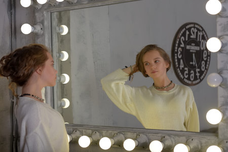 Portrait of a girl in a white sweater in the backlit mirror