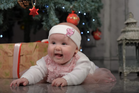 little girl five months in a pink dress lying on the floor by the Christmas tree with giftsの写真素材