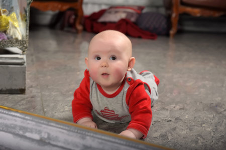 cute newborn baby in red with gray clothes in front of the mirror looks at himself