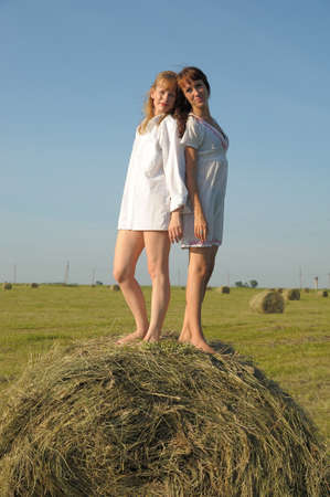 two women in white shirts in a field on a haystackの写真素材
