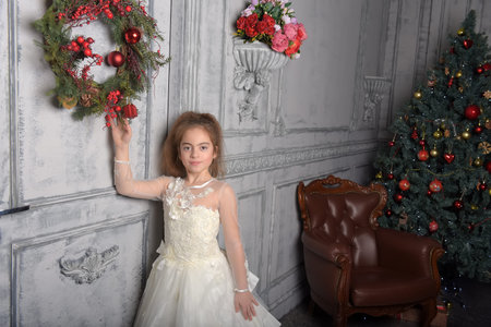 girl in white dress next to christmas wreath on the doorの写真素材