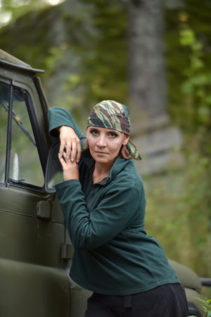 Woman wearing camouflage bandana against the backdrop of UAZ. Fashion, brave.