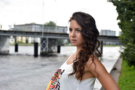 young beautiful brunette girl with curly hair on the background of the bridge in summerの写真素材