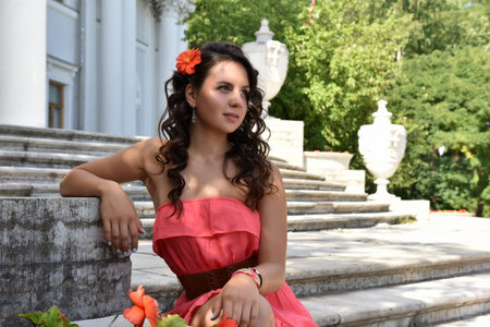 beautiful brunette with curly hair and a pink dress in the summer next to a flower bed