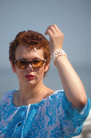 red-haired woman in summer with a short haircut and sunglasses in a blue blouseの写真素材