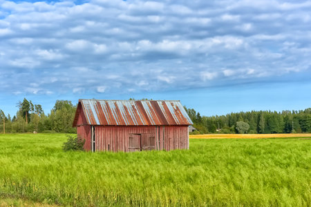 a barn in the middle of a summer field and clouds in the skyの写真素材