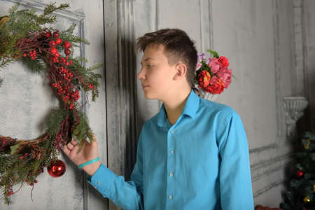 young teenager boy in blue shirt at christmas at the door with christmas wreathの写真素材