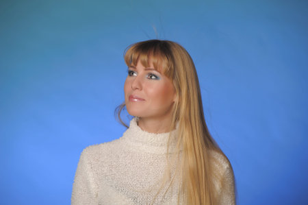 portrait of a beautiful long-haired blonde in a studio on a blue background in a white sweater