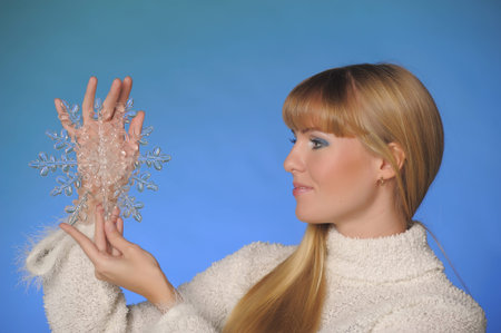 beautiful long-haired blonde in the studio on a blue background with a snowflake in her hands, winter conceptの写真素材
