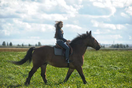 happy girl in jeans rides a horse in a field in summerの写真素材