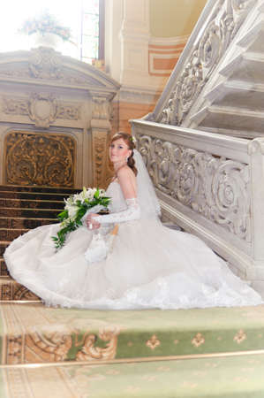 bride with a bouquet in a wedding dress sits on the stairsの写真素材