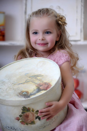 Cute little blonde girl in a pink dress with curls with a vintage big hat box
