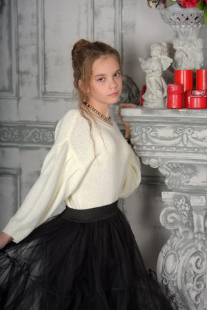 beautiful girl in a white sweater and black skirt by the fireplaceの写真素材