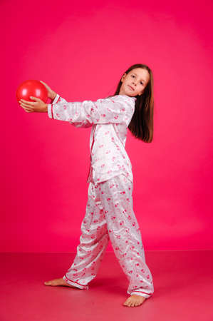 little girl in pajamas with balloons on a pink background in the studioの写真素材
