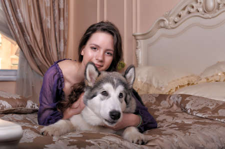 young girl in a lilac dress with her malamute in bedの写真素材