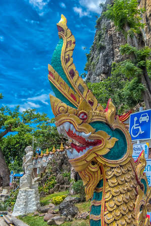Thailand, Phetchaburi 19.07.2019 view of Wat Tham Khao Yoi Cave, Buddhist temple with green tree and rock mountain background, in Phetchaburi, Thailand with Thai text banner means the name of this local is Wat Tham Chao Yoi Cave.のeditorial素材