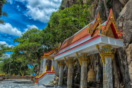 Thailand, Phetchaburi 19.07.2019 view of Wat Tham Khao Yoi Cave, Buddhist temple with green tree and rock mountain background, in Phetchaburi, Thailand with Thai text banner means the name of this local is Wat Tham Chao Yoi Cave.のeditorial素材