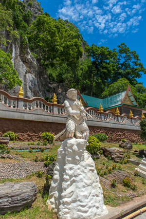Thailand, Phetchaburi 19.07.2019 view of Wat Tham Khao Yoi Cave, Buddhist temple with green tree and rock mountain background, in Phetchaburi, Thailand with Thai text banner means the name of this local is Wat Tham Chao Yoi Cave.のeditorial素材