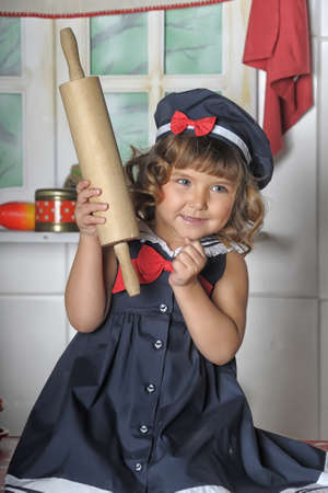 little brunette girl with curls in a marine suit - dress and hat in the kitchenの写真素材