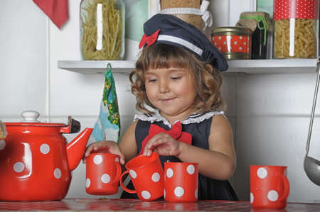 little brunette girl with curls in a marine suit - dress and hat in the kitchenの写真素材