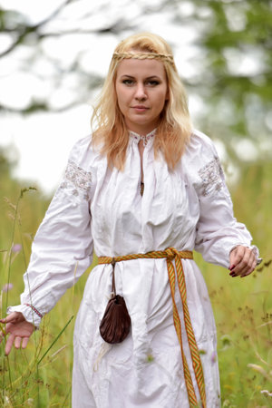 blonde woman in a white slavic shirt among the greenery in summerの写真素材
