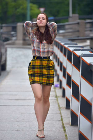 slender pretty brunette girl in a plaid blouse and skirt on a city streetの写真素材
