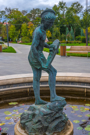 fountain "Boy with a boat" in Sevastopol. This is a bronze sculpture of a boy standing on a rock in the center of a small pond, holding a wooden boat in his hands. The statue symbolizes dreams of the sea, the romance of sailing and the city's connection with maritime history. The composition is surrounded by water lilies, which gives it a special atmosphere.の写真素材