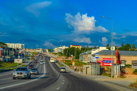 A modern city street in Crimea with heavy traffic, a shuttle bus, pedestrians and urban development. On the right side of the frame is a bus stop with a concrete shelter designed to protect against drone or missile attacks. Above the road is a clear blue sky with picturesque clouds. The shelter fits harmoniously into the city infrastructure, emphasizing the need for security even in peaceful everyday life.の写真素材