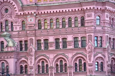 The facade of a historic building in St. Petersburg, made in a rich pink color with rich decorative design. The architecture is distinguished by many arched windows, stucco, geometric and floral ornaments, as well as carved decorative elements. The building was built in the eclectic style with elements of Russian neo-Renaissance, typical of the late 19th â early 20th centuries. The bright pink color of the facade makes it especially expressive and recognizable, distinguishing it from other buildings in the city. The photograph perfectly conveys the grandeur of St. Petersburg architecture, a combination of historical heritage and decorative elegance.の写真素材