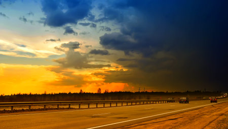 highway against a dramatic sunset. On the left, the sky is bright gold and orange, creating a sense...