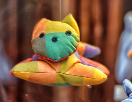 A soft toy in the form of a cat, made of bright fabric with a large checkered pattern. The toy is...