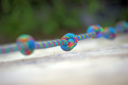 A multi-colored braided cord with knots stretched horizontally. One of the knots, woven from bright...