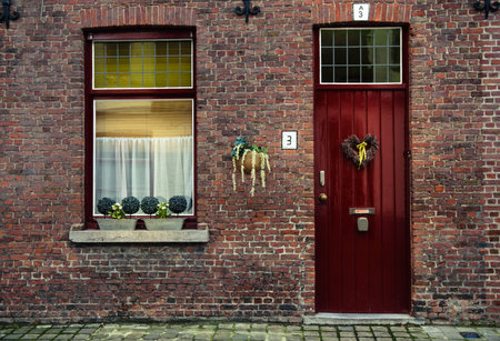 Red wooden window with white curtains and door with heart-shaped wreath. Brick house in Bruges, Belgiumのeditorial素材
