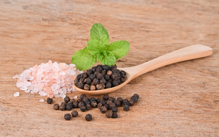 Black pepper in a wooden spoon with pink salt in wooden background