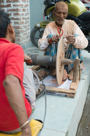 NEPALESE MEN USING HANDMADE TOOL TO SHARPEN SCISSORS OUTSIDE SHOP IN KATHMANDUのeditorial素材