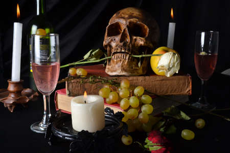 Still life with a skull with roses, books, fruit, wine and candles on a dark backgroundの写真素材
