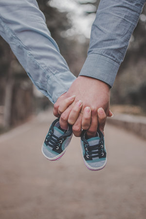 A woman and a man hold the baby's shoes. A woman and a man hold children's shoes on the meadow in the open air. Waiting for a baby conceptual image. Family love.の写真素材