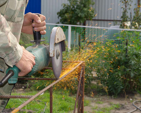 Angle Grinder Metal sawing with flashing sparks close up and Repairman hands home repair garden working summer time  Also called Circular Saw handheld electric instrumentの写真素材