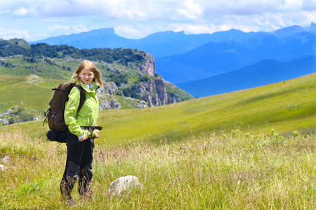 Woman Hiker with Backpack standing Outdoor on green Valley Grass and Mountains rocks on background Summer Dayの写真素材