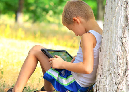 Boy Child playing with Tablet PC sitting on skateboard Outdoor with forest on background Game Dependence conceptの写真素材