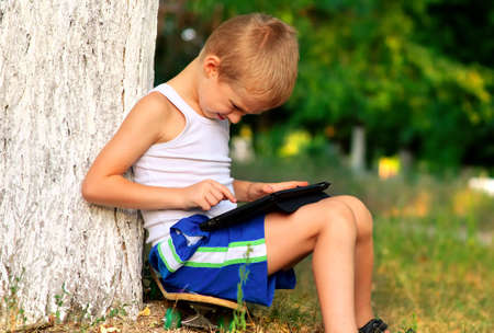Boy Child playing with Tablet PC Outdoor with forest on background Computer Game Dependence conceptの写真素材