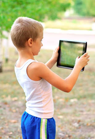 Boy Child playing with Tablet PC standing Outdoor with nature on background Computer Game Dependence conceptの写真素材
