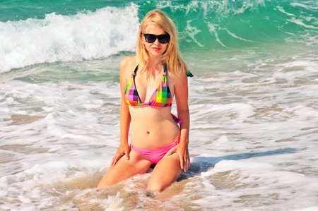 Young Woman in bikini swimwear sitting on Beach Seaside resort with blue Sea Waves on background Summer Travelの写真素材