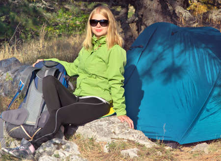 Young Woman with Smiling Face Hiker sitting with backpack and Tent Camping Outdoor on Grass with forest nature on background Travel and Healthy Lifestyle conceptの写真素材