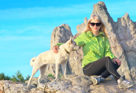 Smiling Woman Traveler and white dog sitting on stones relaxing with Rocky Mountain peak Ai-Petri and blue sky on Background Traveling Climbing conceptの写真素材