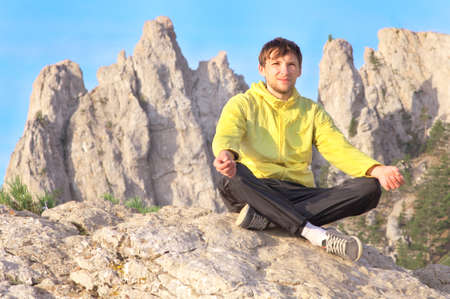 Man Traveler Relaxing Yoga Meditation sitting on stones with Rocky Mountains peak Ai-Petri and blue sky on Backgroundの写真素材