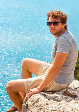 Young Man relaxing Outdoor on rocky cliff sitting and looking on Sea Summer time Traveling Lifestyleの写真素材