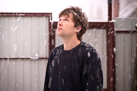 Young Man in sweater looking up on falling Snowflakes Outdoor Winter season Snowing weather trendy styleの写真素材