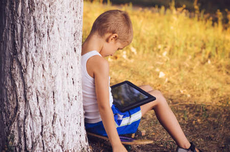 Boy Child playing with Tablet PC Outdoor with Summer nature on background Computer Game Dependence concept Lifestyleの写真素材